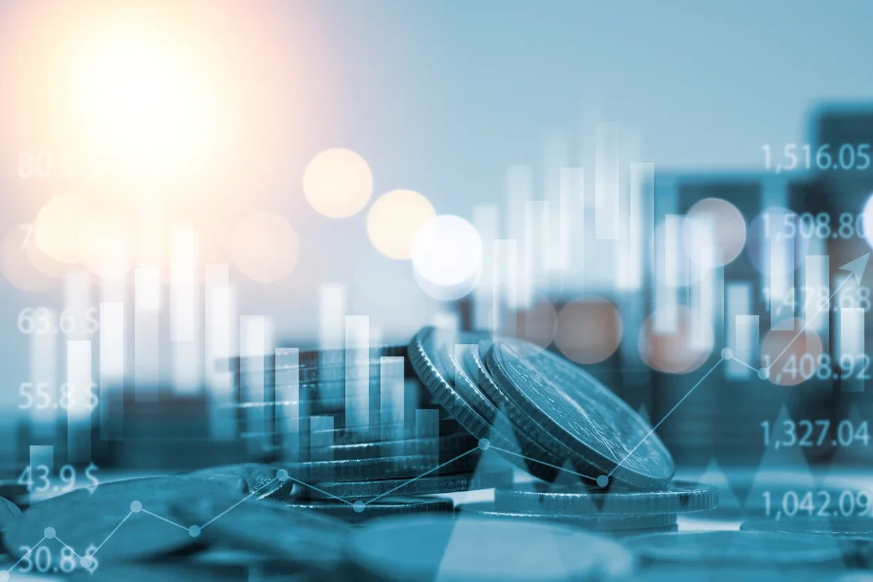 Imagem de um computador com gráficos e números financeiros sobrepostos, ao lado de uma caneta e um smartphone, sugerindo análise de dados e regime tributário