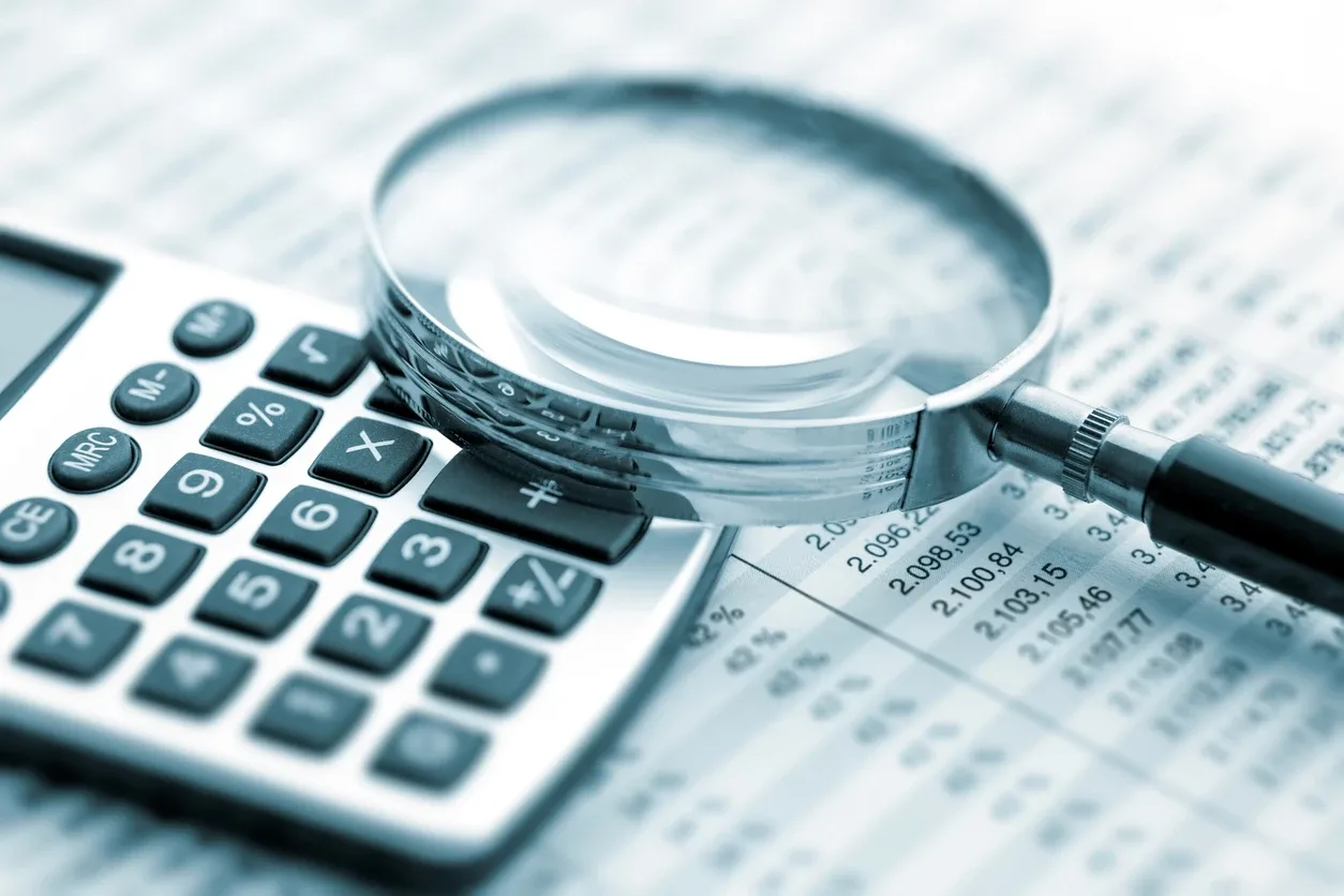 Conciliação financeira na Reforma Tributária: lupa sobre calculadora e planilha com números e gráficos, representando análise de dados contábeis e contas.