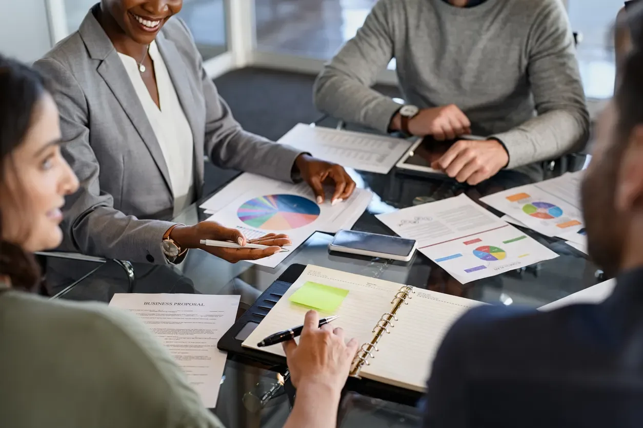 Demonstrações financeiras consolidadas: Equipe reunida em reunião corporativa analisando relatórios e gráficos em papéis e tablet, enquanto discute resultados financeiros e planejamento