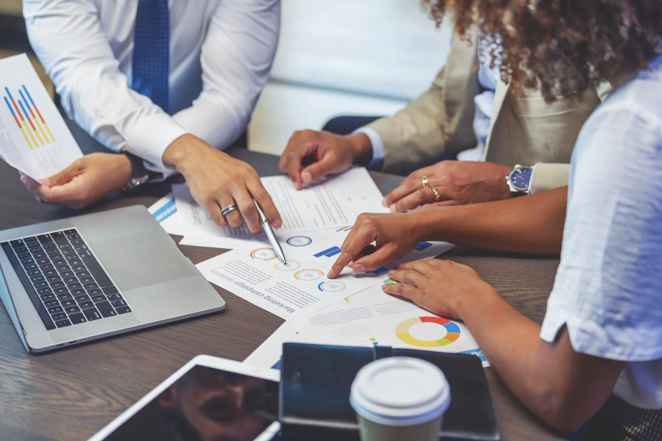 Profissionais analisando gráficos e documentos financeiros sobre uma mesa, com laptop e café, durante reunião de planejamento de despesas em uma startup.