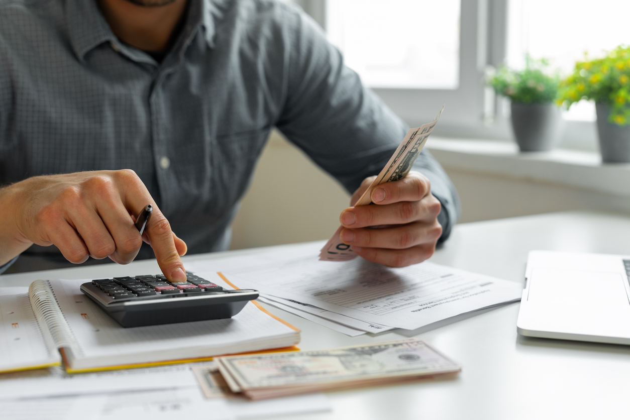 Pessoa calculando finanças, calculadora e documentos sobre a mesa, representando a gestão de recebimentos recorrentes.