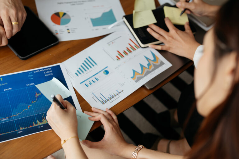 Reunião de profissionais analisando relatórios financeiros e gráficos de lucro operacional em uma mesa de trabalho.