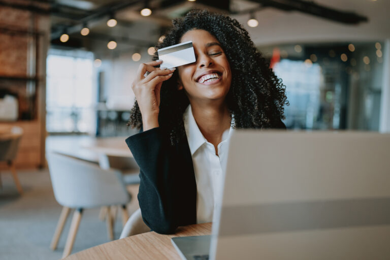 Mulher sorridente segurando um cartão de crédito enquanto realiza uma compra online em ambiente moderno. Ideal para discutir política de crédito e empréstimos.