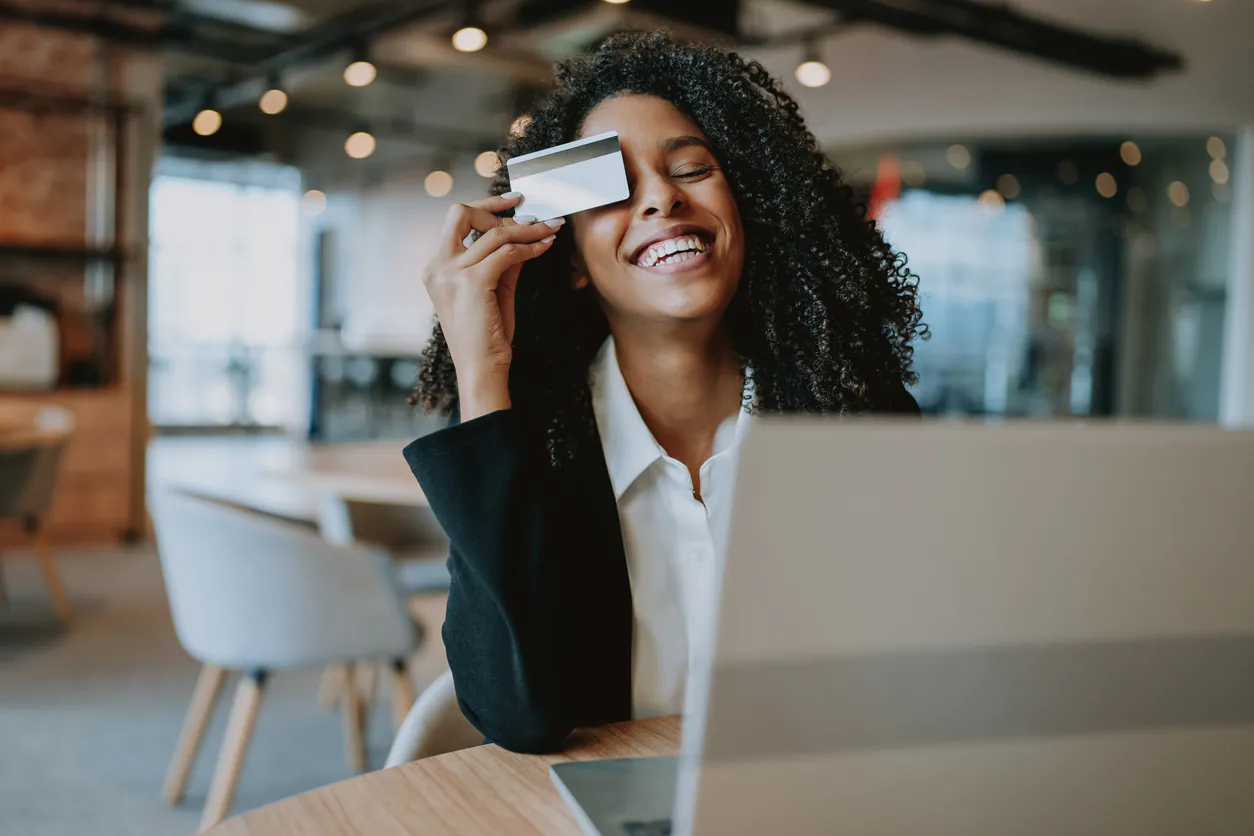 Mulher sorridente segurando um cartão de crédito enquanto realiza uma compra online em ambiente moderno. Ideal para discutir política de crédito e empréstimos.