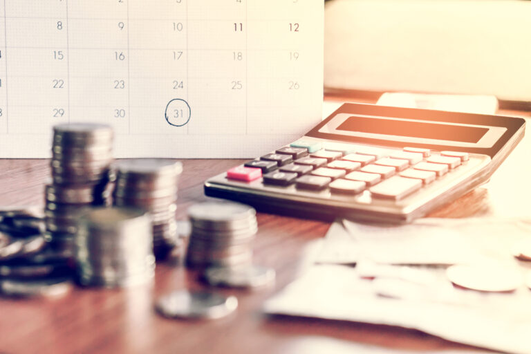Imagem de uma calculadora financeira ao lado de pilhas de moedas, uma agenda marcada e papéis, simbolizando gestão financeira e o prazo médio de recebimento.