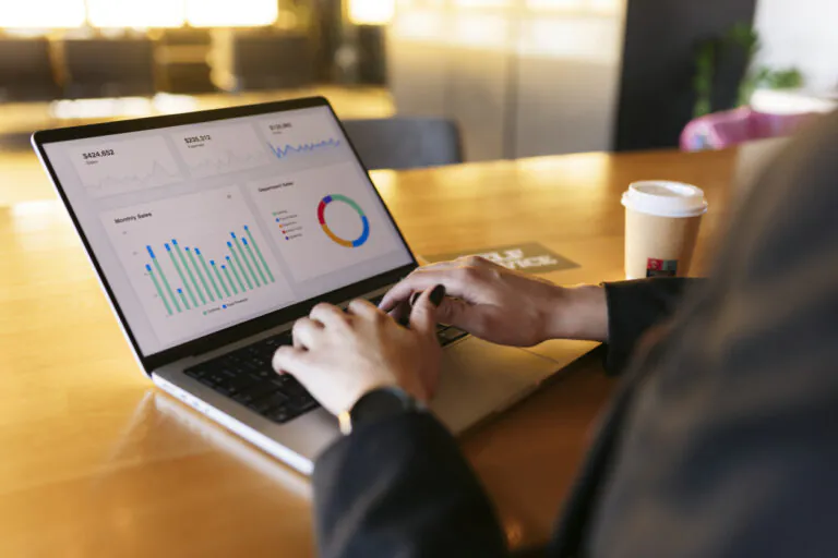 Pessoa analisando relatórios financeiros customizáveis em um laptop na mesa de um escritório com café ao lado