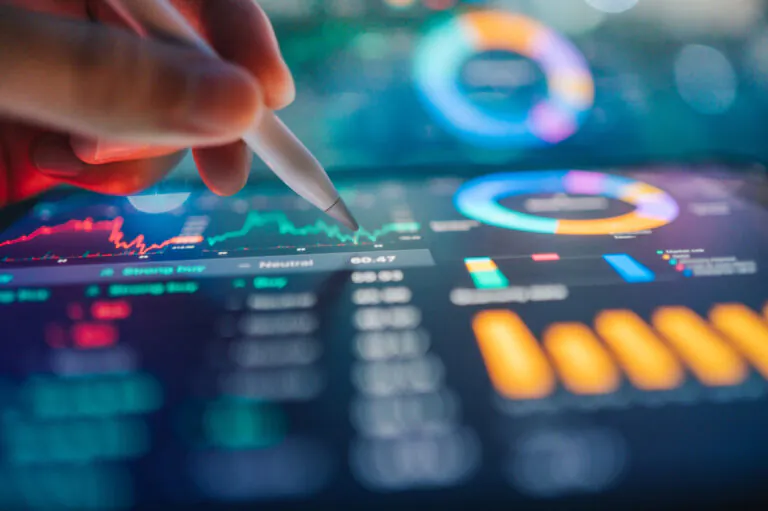 Aplicativo de despesas: dedos usando uma caneta sobre tela com gráficos e indicadores financeiros, incluindo barras, números e curva de tendência desfocada, sugerindo controle e planejamento de gastos.