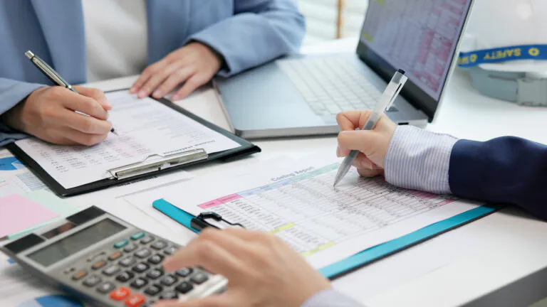 Profissionais analisando planilhas financeiras e calculando custos em uma mesa de trabalho, com calculadora e documentos para discutir capex e opex.