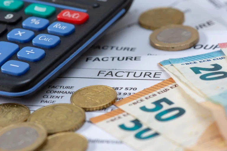 Melhores contas PJ: Calculadora ao lado de documentos de fatura, com moedas e cédula de 50 reais sobre papel, representando planejamento financeiro e contas empresariais.